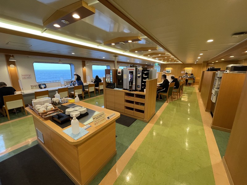 Long view of the Ferry Soleil restaurant interior with cutlery and crockery island, self-service drinks area, and rows of seats looking out at the sea