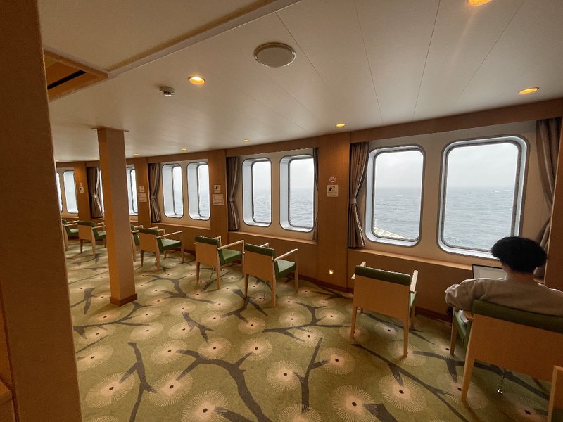Front-facing lounge  with armchairs looking through windows out at the sea in the direction of travel on the Ferry Soleil, Japan