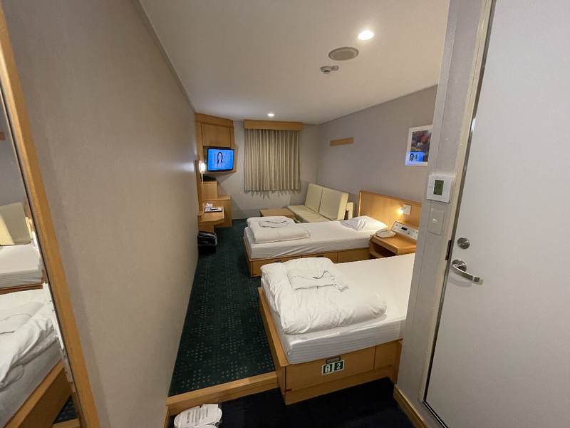 Private state room with twin beds, sofa, TV and door to en-suite bathroom, as well as curtained porthole on the Ferry Soleil, Japan