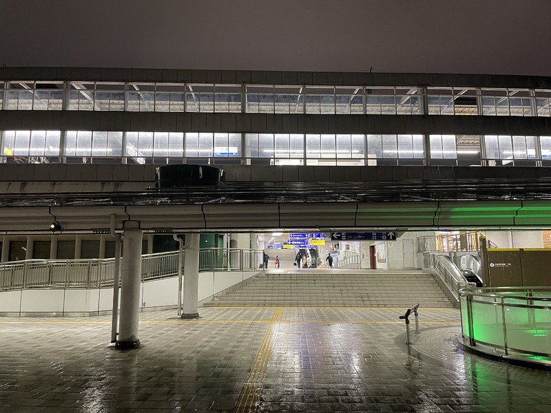 A view of the entrance to Kokura Station on a rainy night with the brightly-lit platforms overhead