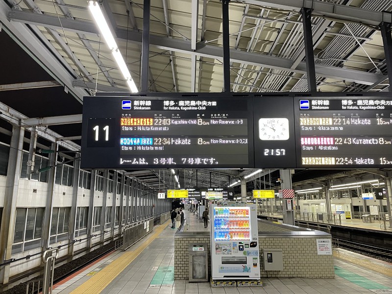 A long view of platforms 11 and 12 in Kokura Station with overhead departure boards