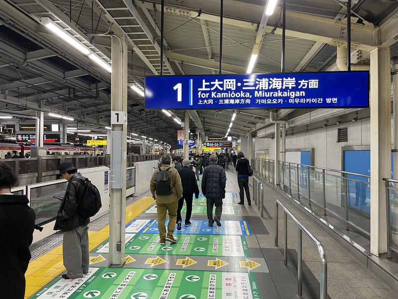 Long view of passengers on platform 1 on the Keikyo Line at Yokohama Station, with overhead signage and information on the platform floor