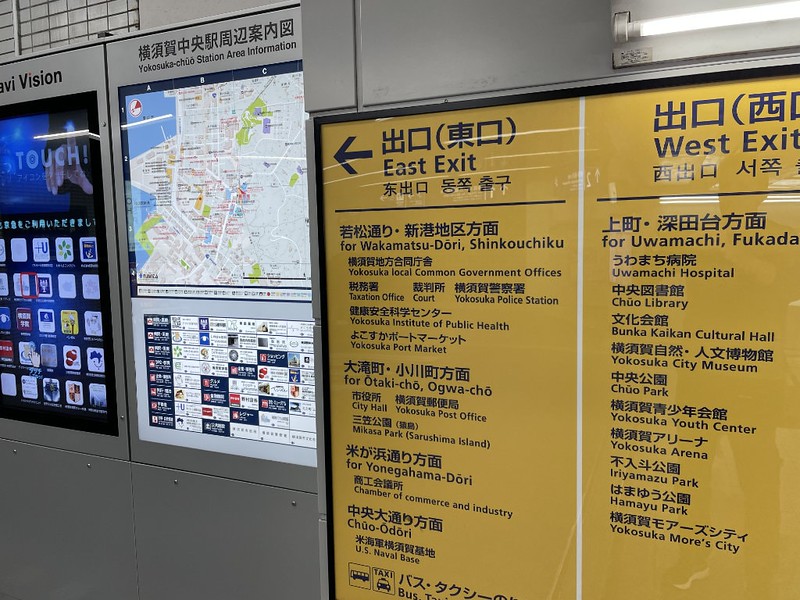 Yellow station exit information signs at Keikyu Yokosuka-chuo Station, with details of local landmarks beyond the east and west exits
