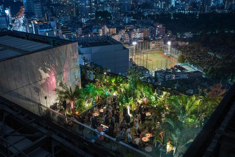 View over The Aoyama Grand Hotel rooftop bar with tall plants and wall projections and a nighttime city view of Tokyo