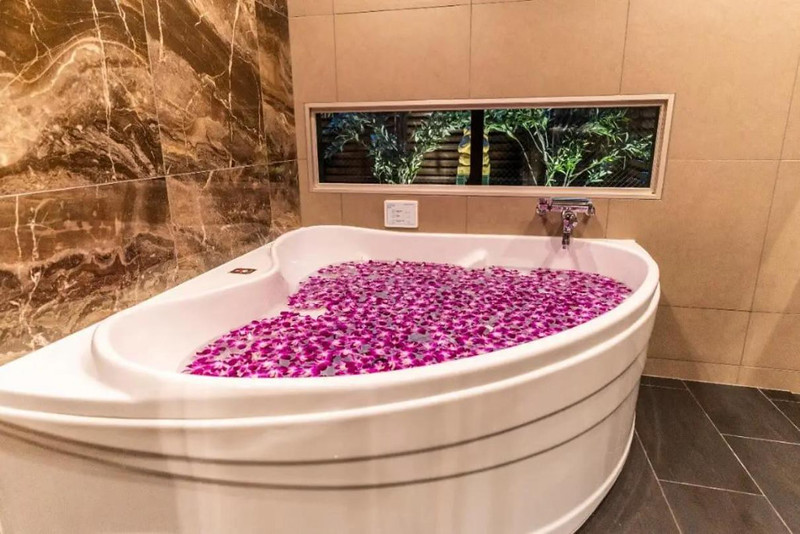 Bathtub full of water and layered with pink petals, as well as window view of trees outside, in the BaliAn Resort Forest Ikebukuro, Tokyo, Japan