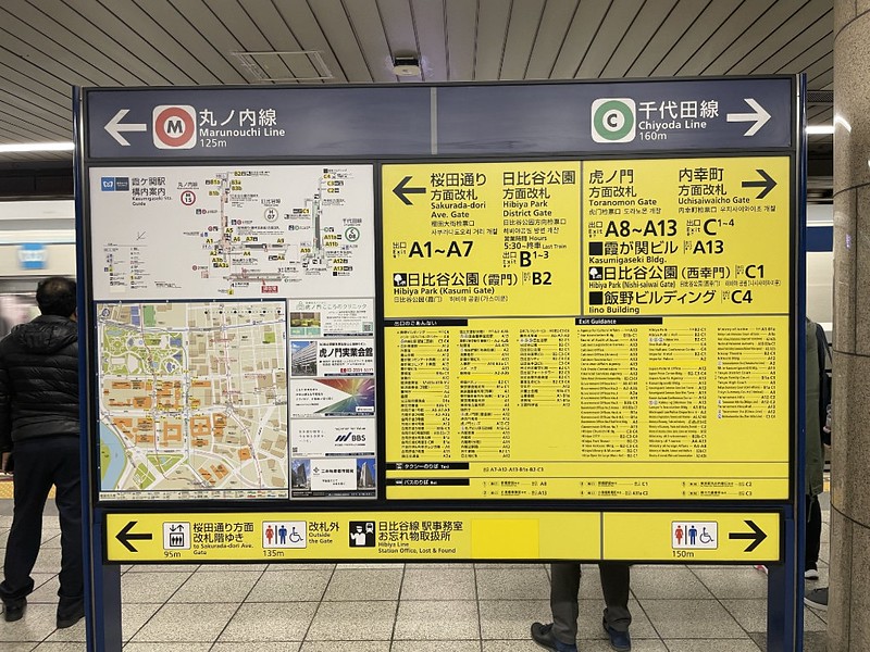 An example of a yellow and black branded exit information board in a Tokyo train station, with maps and schematics of the station and local area, in addition to directions for facilities and local landmarks