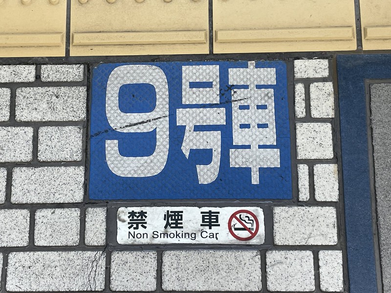 Blue numbered sign on the floor of a train station platform, showing which car stops at that point for boarding, as well as information about whether it is a smoking car or not