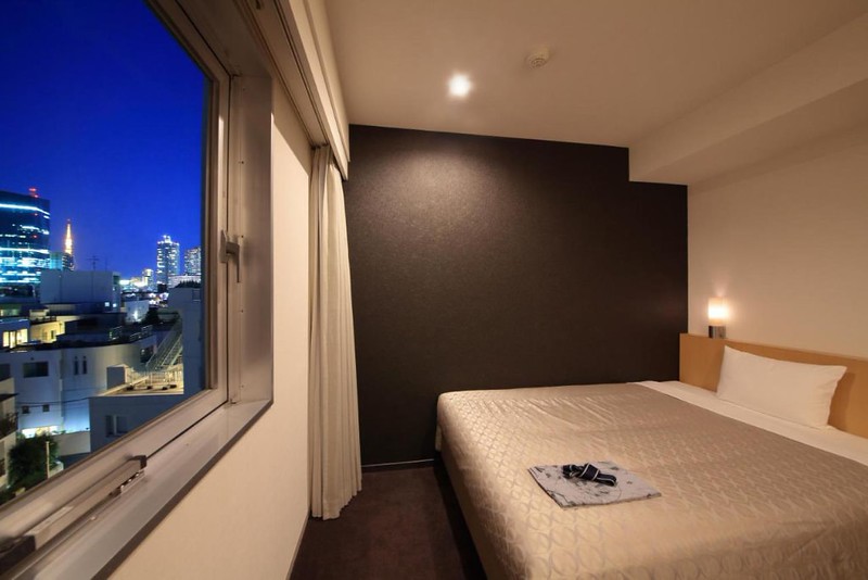 Simple double guest room in the Hotel Asia Center of Japan, Tokyo, with large double bed facing a wide window overlooking the city at night