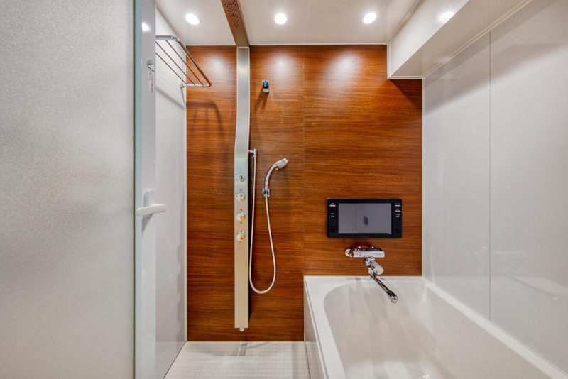 Guest room bathroom in the Hotel Lotus, Tokyo, Japan, with bathtub and shower unit, and TV screen