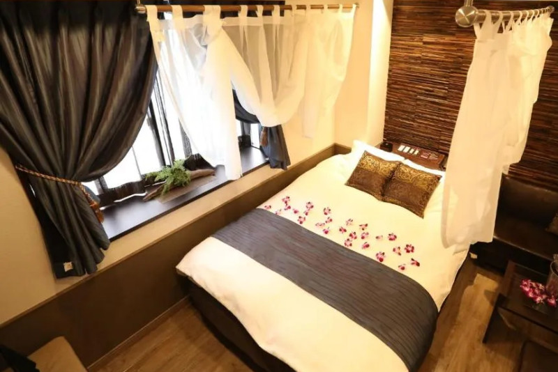 Non-smoking guest room in the Hotel PetitBali Higashi-Shinjuku, Tokyo, Japan, with a double bed surrounded by curtains and Champagne on ice on the side table