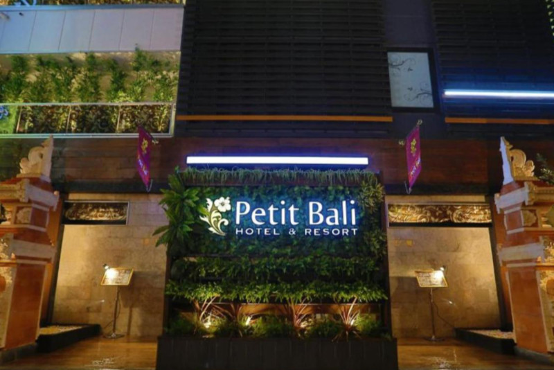 Exterior of the Hotel PetitBali Higashi-Shinjuku, Tokyo, Japan, on a rainy night, with the name of the hotel illuminated and plant features