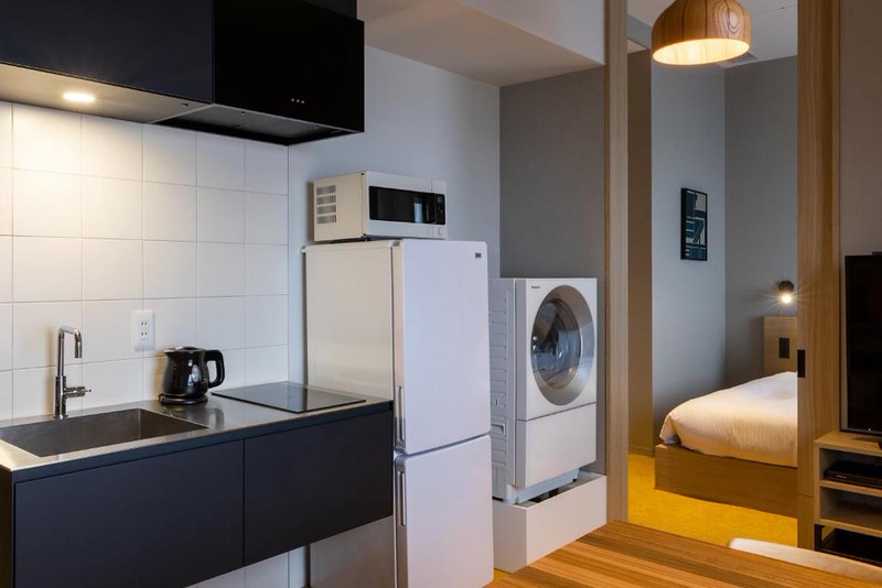The kitchen and laundry facilities in the Hundred Stay Tokyo Shinjuku hotel with sink and hob area, fridge and microwave, and washing machine