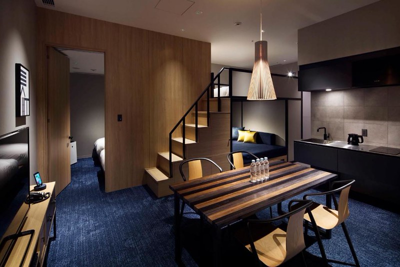 A superior quad room in the Hundred Stay Tokyo Shinjuku hotel with dining table, kitchen area, and stairs to a loft bed