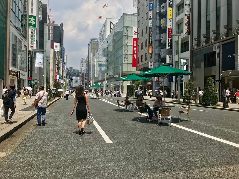A view from the road of Tokyo’s Chuo-dori Street, lined by famous brand stores, and with chairs, tables, and umbrellas for visitors to sit running down the centre of the traffic-less street