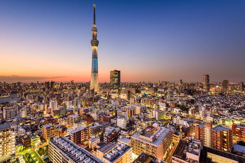 An illuminated Tokyo Skytree towers above surrounding buildings in early evening