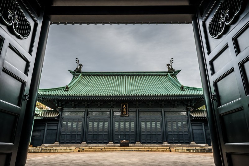 View through the heavy wooden doors into the main courtyard of Yushima Seido temple in Tokyo, Japan, with its distinct curved, green roof