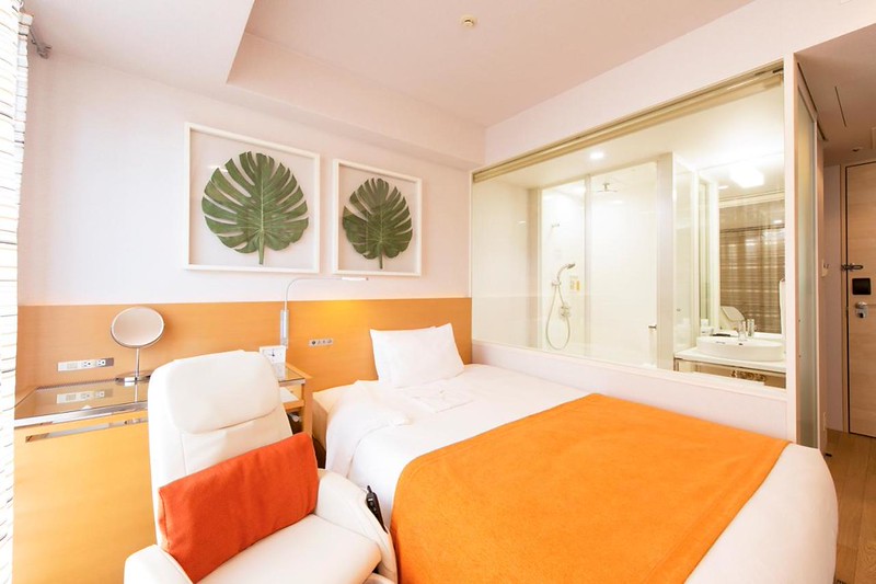 A guest room in the Remm Hibuya hotel, Tokyo, Japan, with orange interiors, bed, shower room, and massage chair