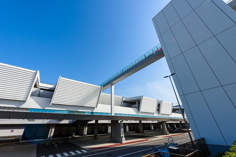 View from the street of the road and buildings of the Toyosu fish market in Tokyo with a gantryway connecting different parts on a bright, clear day