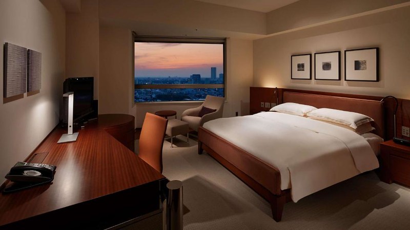 Broad double bed with desk area and window easy chair overlooking the Tokyo skyline at dusk in a Grand Hyatt hotel guest room Broad double bed with desk area and window easy chair overlooking the Tokyo skyline at dusk in a Grand Hyatt hotel guest room