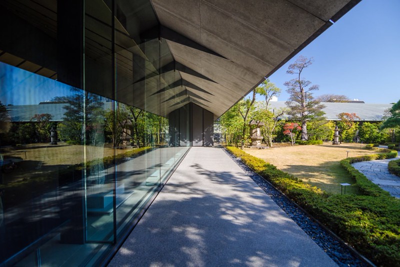 Exterior of Nezu Museum to the left, with pathway and canopy, and windows reflecting the Japanese Garden to the right, in Tokyo, Japan