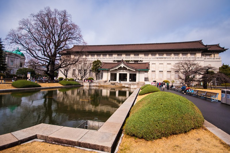 Long view of the main building at Tokyo National Museum with the square pond in front and people walking on the pathways towards the museum