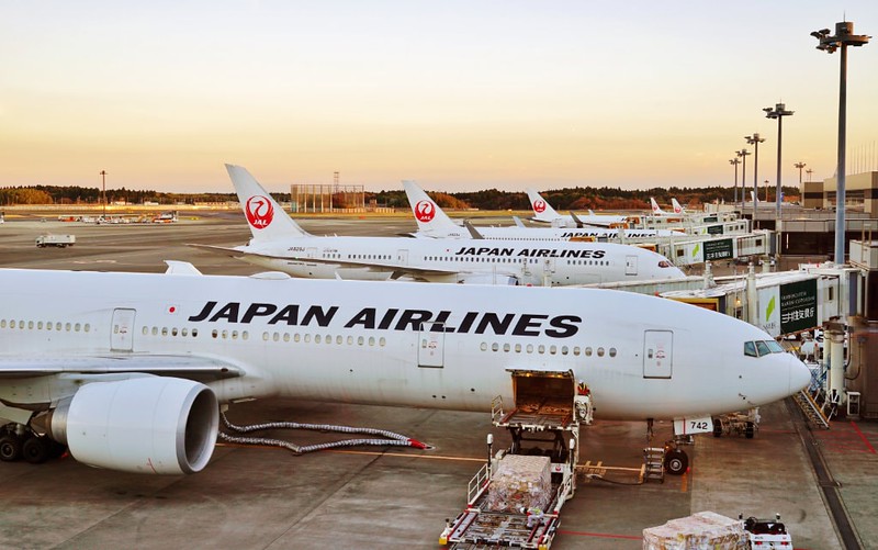 A row of Japan Airlines planes sit next to one another at Narita International Airport at twilight A row of Japan Airlines planes sit next to one another at Narita International Airport at twilight