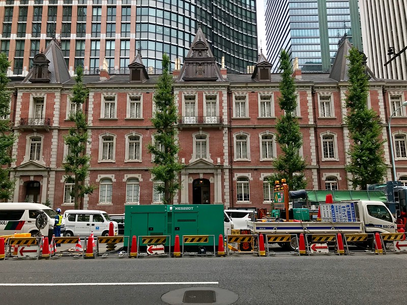 The distinctive red-brick façade and entrance to the Mitsubishi Ichigokan Museum in Tokyo, Japan, with roadworks in front and a line of skyscrapers behind