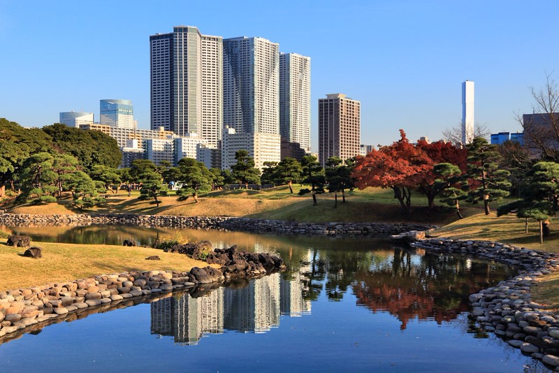Tokyo’s skyscraper skyline and green foliage reflected in the water in Hamarikyu Gardens