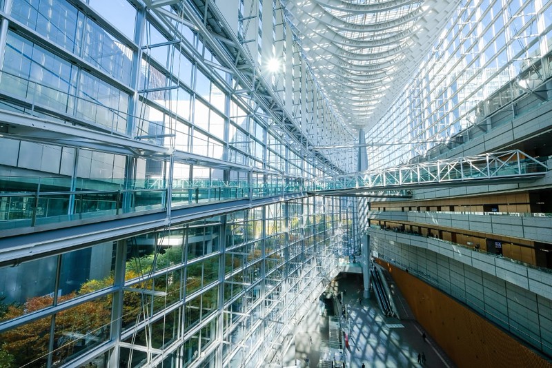 Interior view of the main atrium of the Tokyo International Forum Building, with a tall wall of windows, glass roof, and gantryways