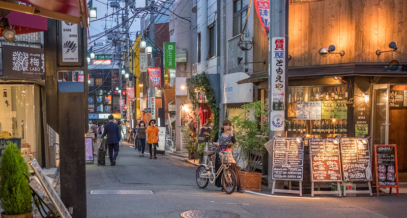 Local residents walk past shops, bars, and restaurants in an alley at twilight in the Shimokitazawa district of Tokyo, Japan