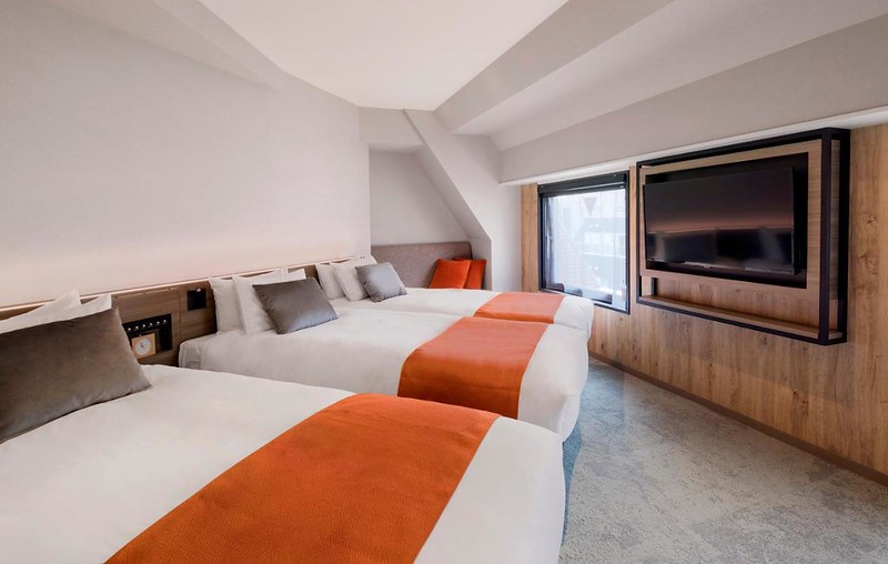 Angular triple guest room in the b Tokyo Ochanomizu hotel, Tokyo, Japan, with three large beds and large TV