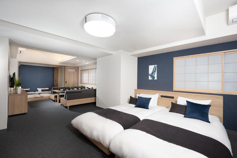 Family room in the Mimaru Tokyo Shinjuku West hotel, Tokyo, Japan, with two sets of twin beds, long dining table with sofa seating, and contemporary update on traditional minimal Japanese style