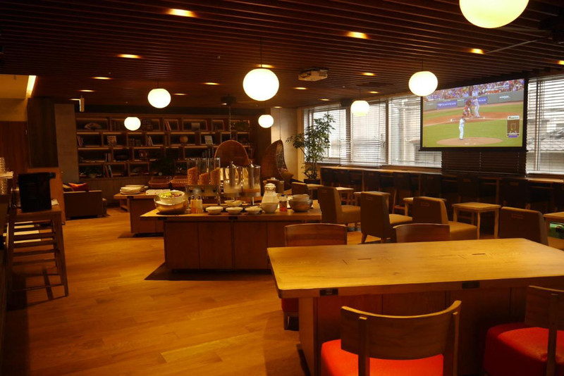 Lobby and dining area of the MyCUBE by MYSTAYS Asakusa Kuramae hotel in Tokyo, Japan, with chairs and tables, and island with food, and TV