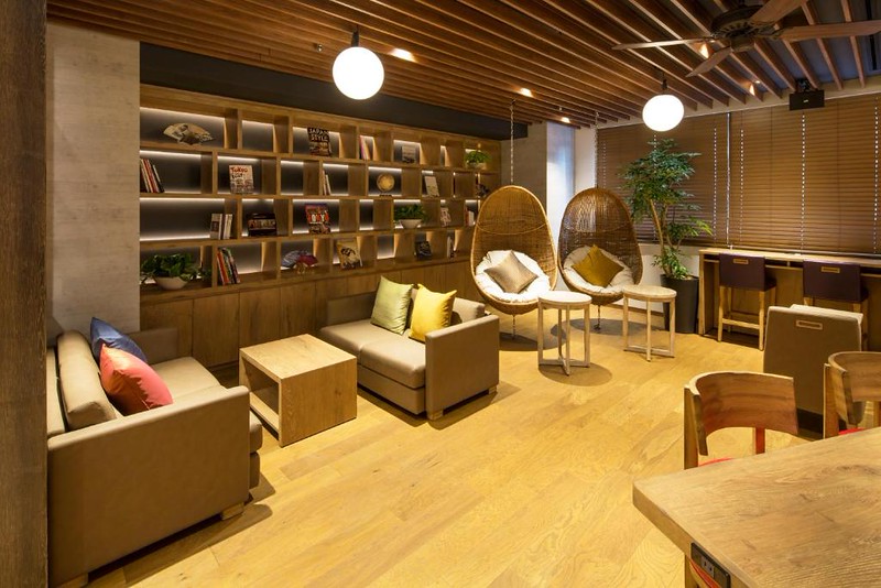 Modern lounge area in the MyCUBE by MYSTAYS Asakusa Kuramae capsule hotel, Tokyo, with sofas, wooden bookshelves, and hanging wicker chairs