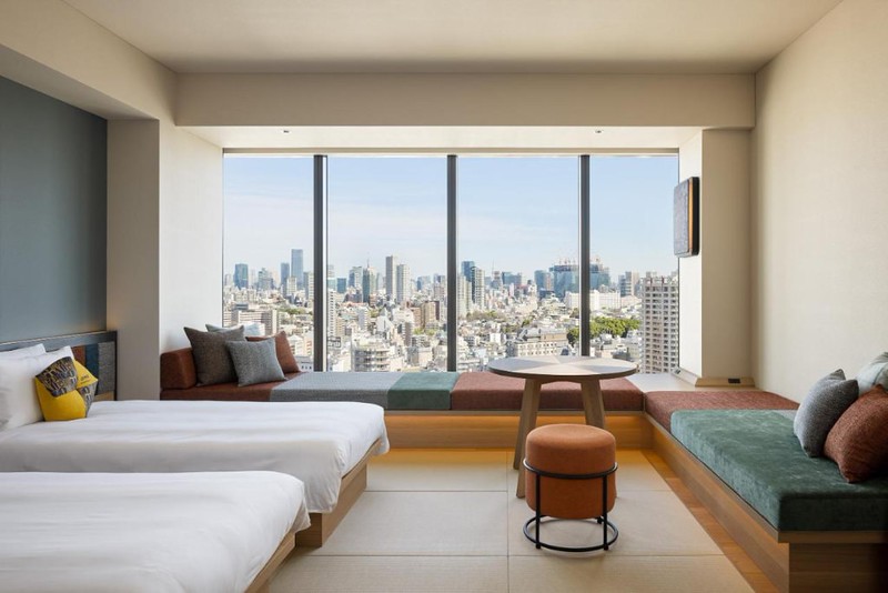 Twin guest room in the OMO5 Tokyo Gotanda by Hoshino Resorts with wall-length windows and corner window-length sofa