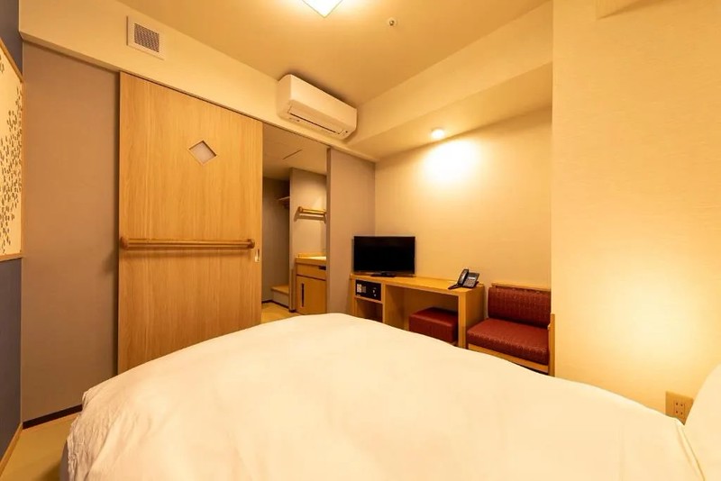 View from the bed of a compact guest room in the Onyado Nono Asakusa Bettei hotel, Tokyo, with small desk and chair and view through to bathroom sink