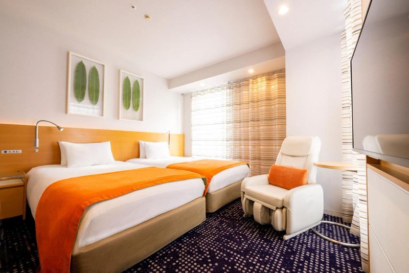 Compact twin guest room in the Remm Hibiya Hotel, Tokyo, Japan, including two beds with orange styling, relaxing chair, purple dotted carpet, and curtained window