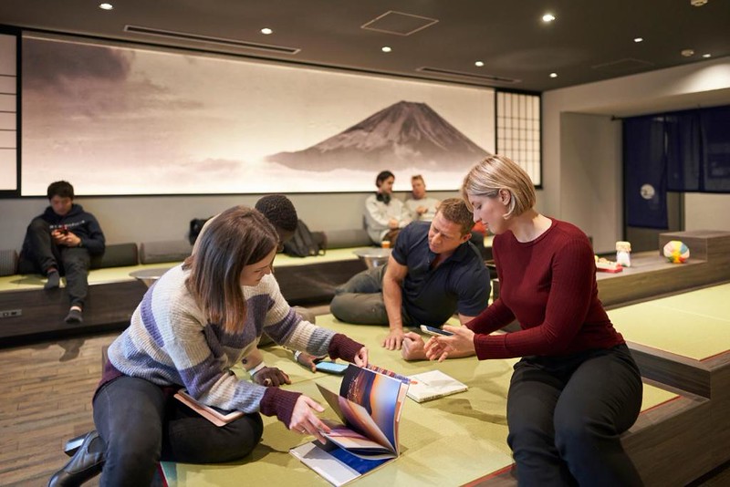 Groups of people gather around guide books and phones in the lounge of the Resol Poshtel Tokyo Asakusa capsule hotel