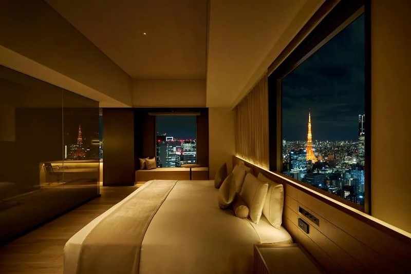 Double guest room in the Royal Park Hotel the Shiodome, Tokyo, Japan, with wide double bed sat beneath the wall-length corner windows, overlooking the city at night, and reflected in the gold-effect wardrobe doors