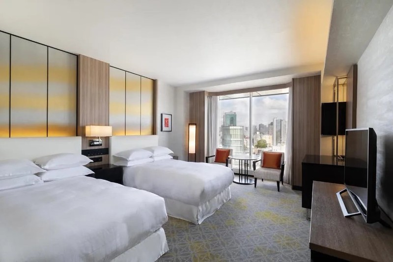 Twin guest room in the Sheraton Miyako Hotel Tokyo, with two wide beds and dining area beside balcony window