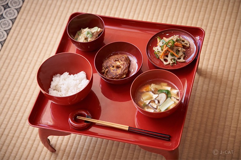Five small red laquer dishes containing portions of shojin ryori or Japanese Buddhist cuisine sit on a red laquered tray table on a tatami mat