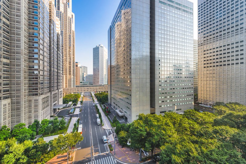 View of street and high-rise buildings past the Metropolitan Government Building in West Shinjuku, Tokyo on a sunny day View of street and high-rise buildings past the Metropolitan Government Building in West Shinjuku, Tokyo on a sunny day