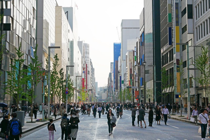 A street scene in Ginza, Tokyo, Japan, with pedestrians walking along in the middle of the road between the tall buildings