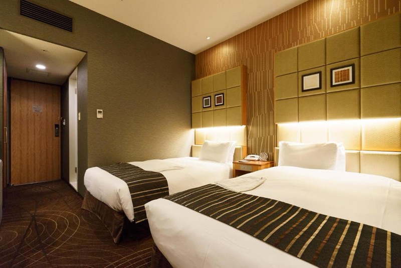 Twin guest room in the Sotetsu Fresa Inn Higashi Shinjuku, Tokyo, Japan, with padded headboards and strip lighting above the pillows, brown carpet with sprial geometric patterns
