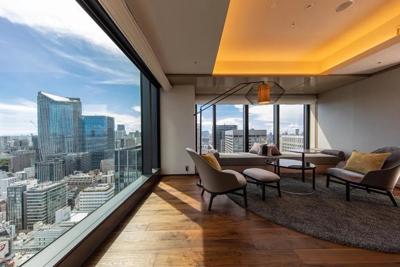 Comfortable living area with chairs and table and a panoramic city view of Tokyo from the huge corner windows in a suite in The Blossom Hibiya hotel, Tokyo, Japan