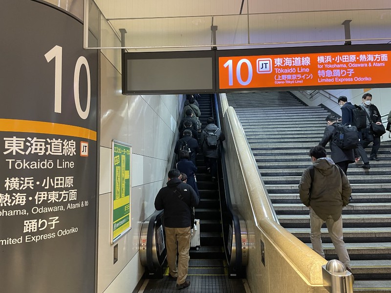 Orange illuminated sign and sign affixed to the wall, pointing up the stairs and escalator to the Tokaido Line in Tokyo Station