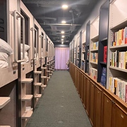 A corridor of double-decker sleeping capsules on the left with shelves of books for guests to read on the right in the Book Tea Bed Shibuya capsule hotel, Tokyo