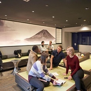 Groups of people gather around guide books and phones in the lounge of the Resol Poshtel Tokyo Asakusa capsule hotel
