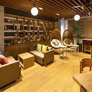 Modern lounge area in the MyCUBE by MYSTAYS Asakusa Kuramae capsule hotel, Tokyo, with sofas, wooden bookshelves, and hanging wicker chairs