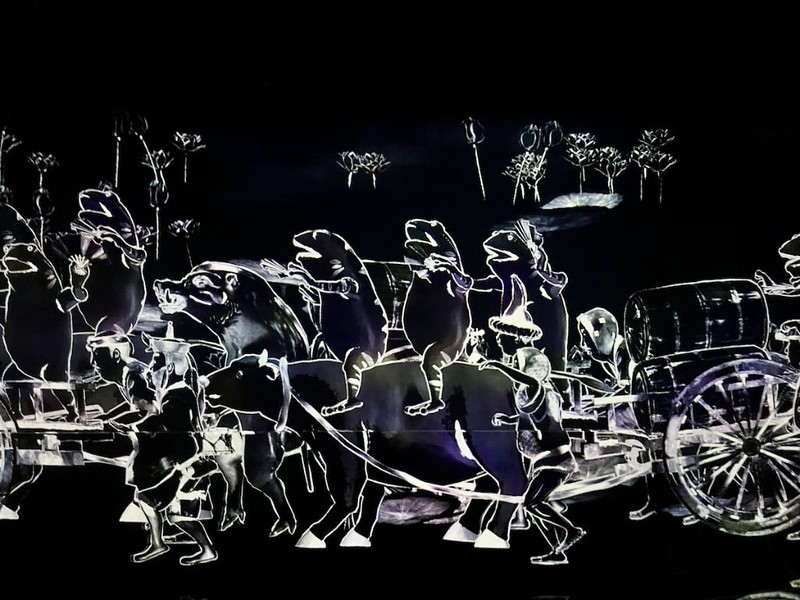 An artwork with a parade of frogs slowly marching along the walls in one of the hallways of teamLab Borderless